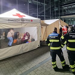 Zelt des BRK bei Ukraine-Hilfe-Einsatz mit Einsatzkräften und Menschen in der Nacht vor einem Gebäude