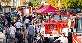 Menschenmenge beim Tag der offenen Tür der Abteilung Harthof mit roten Feuerwehrfahrzeugen und Pavillons in einer Straße mit herbstlichen Bäumen