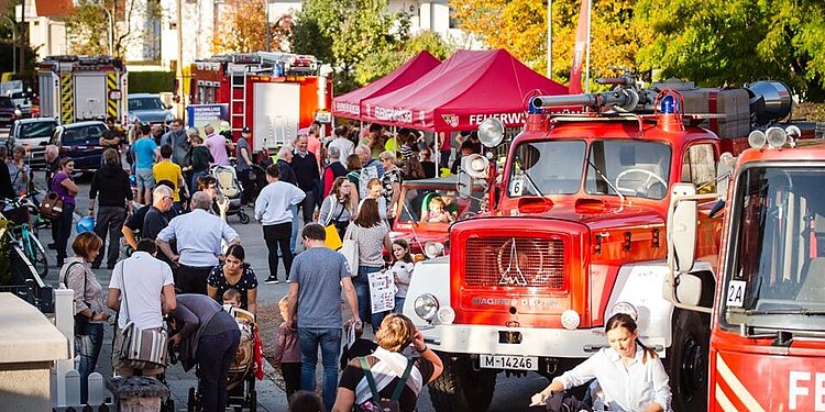 Menschenmenge beim Tag der offenen Tür der Abteilung Harthof mit roten Feuerwehrfahrzeugen und Pavillons in einer Straße mit herbstlichen Bäumen