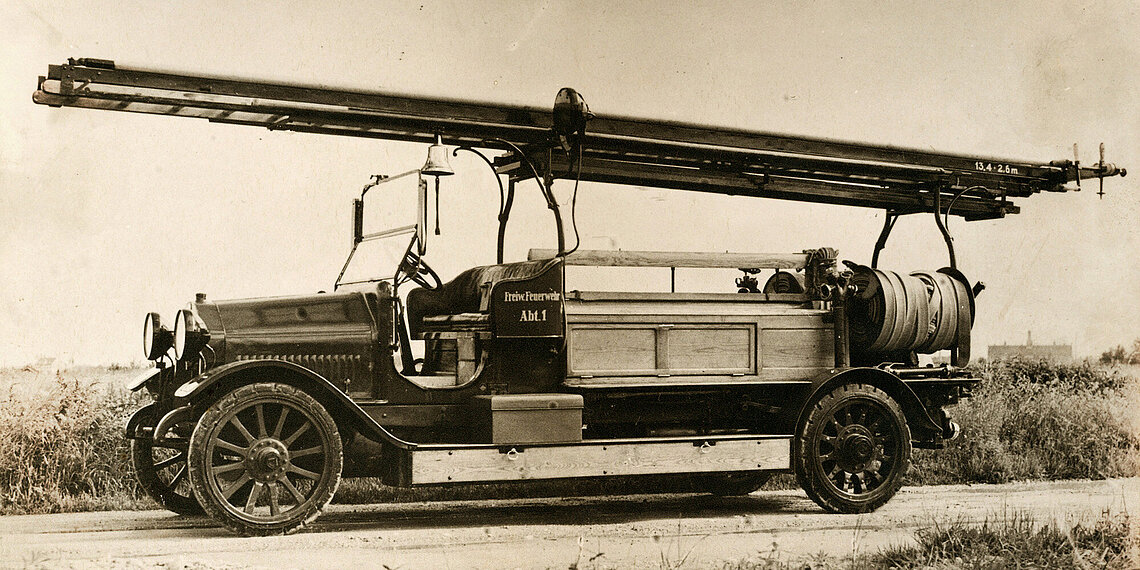 Historische Motorspritze von Saurer mit langer Leiter auf einem Dachgestell und offenem Fahrersitz auf Feldweg