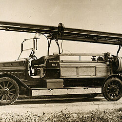 Historische Motorspritze von Saurer mit langer Leiter auf einem Dachgestell und offenem Fahrersitz auf Feldweg