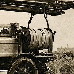 Historische Motorspritze von Saurer mit langer Leiter auf einem Dachgestell und offenem Fahrersitz auf Feldweg