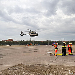 Polizeihubschrauber schwebt über der Theresienwiese, Flughelfer in Schutzkleidung stehen in Bereitschaft