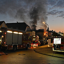 Brennendes Wohnhaus mit Rauchwolken und Löscharbeiten im Morgengrauen