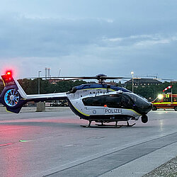 Polizeihubschrauber auf der Thereseinwiese bei Dämmerung, im Hintergrund der Einsatzleitwagen der Flughelfer mit eingeschaltetem Licht