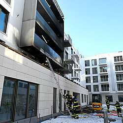 Feuerwehrleute in Schutzkleidung bei einem Brandeinsatz an einem modernen Wohngebäude mit deutlichen Brandspuren mit Leitern und Ausrüstung
