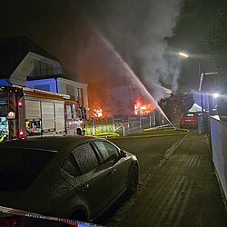 Brennendes Wohnhaus mit Löscharbeiten bei Nacht