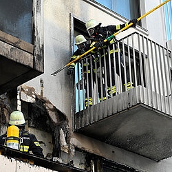 Feuerwehrleute in Schutzkleidung und Helmen bei Löscharbeiten am Balkon eines Gebäudes