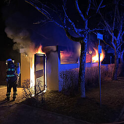 Feuerwehrleute löschen nachts einen Brand eines Müllhauses, Flammen und Rauch sind zu sehen