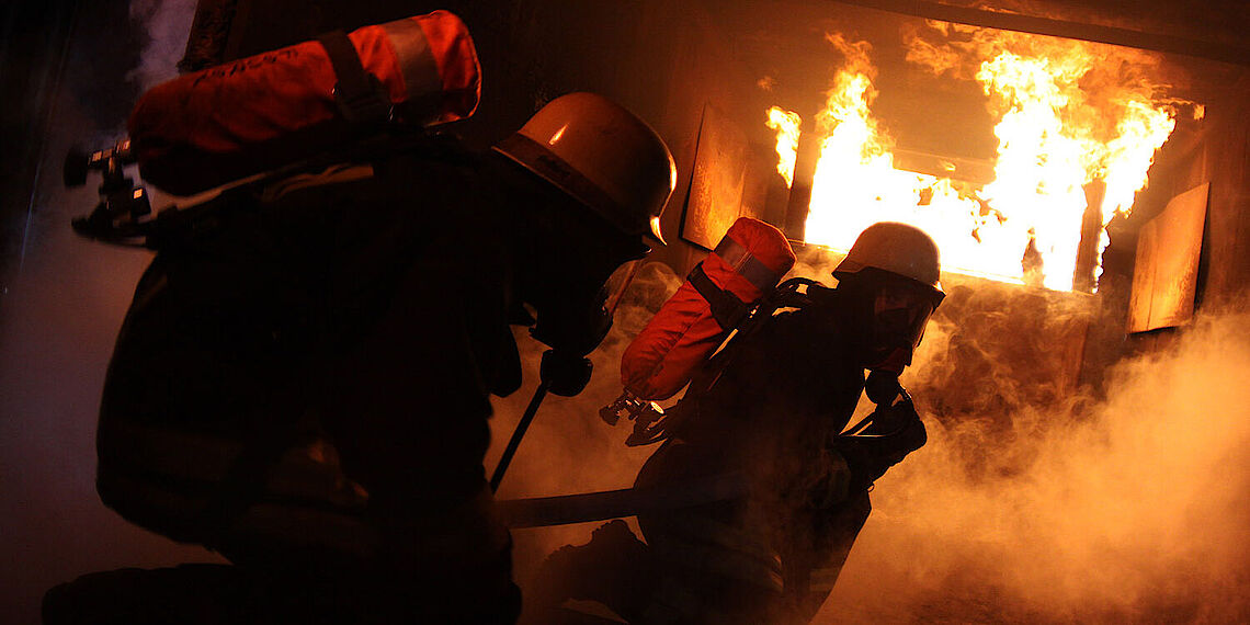 Zwei Feuerwehrleute unter Atemschutz bei einer Brandübung mit Flammen und Rauch